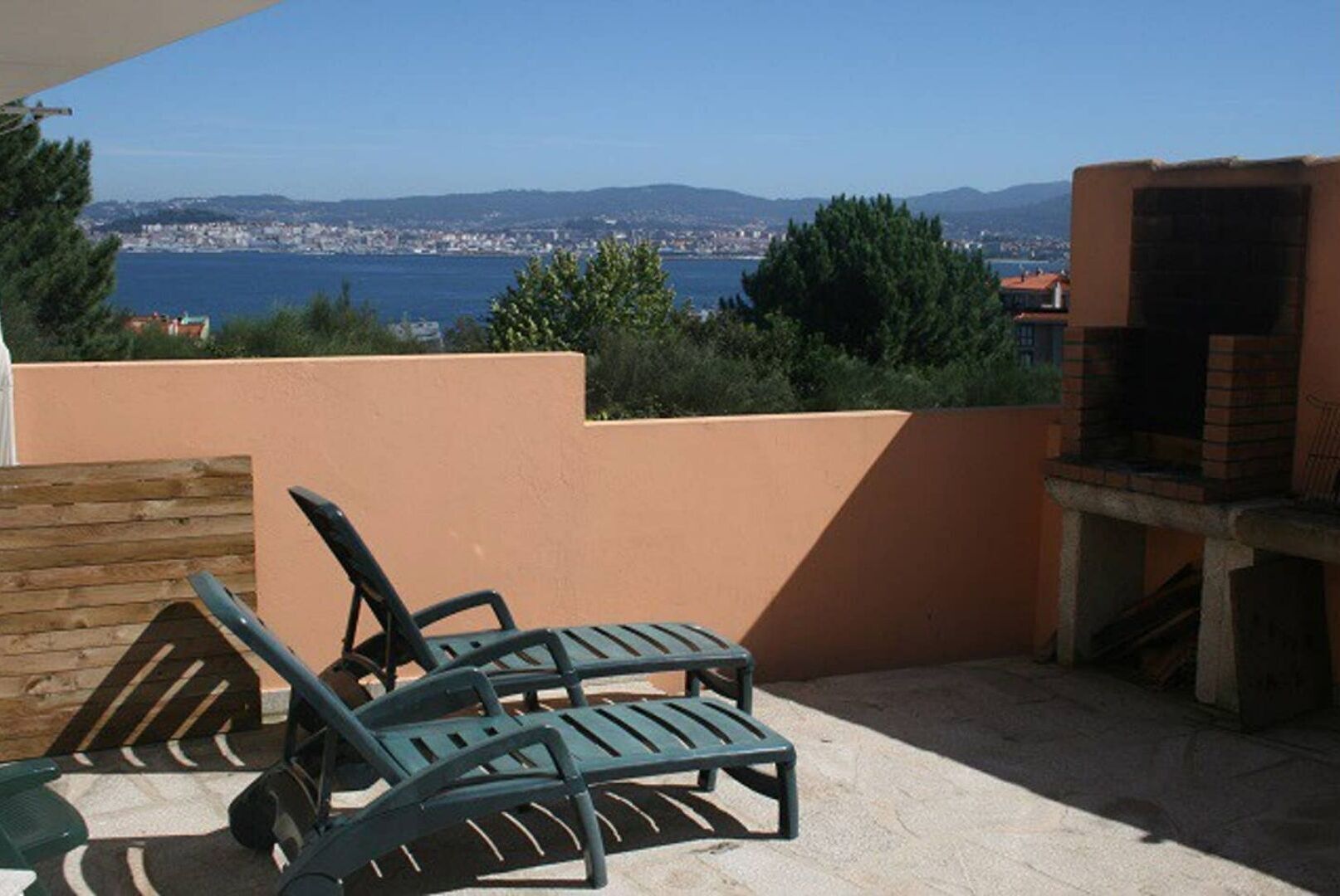 Une terrasse avec deux chaises longues, un barbecue et une vue sur une ville côtière.