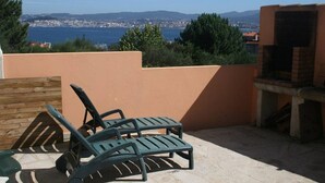 Een terras met twee loungesteilen, een barbecue en uitzicht op een kustplaats.