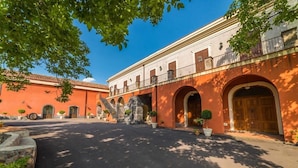 A courtyard with a stone staircase leading to an upper level, surrounded by buildings with arched doorways and potted plants.