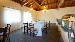 A dining area with a long table set for six, wooden chairs, stone flooring, and a wooden ceiling with exposed beams.