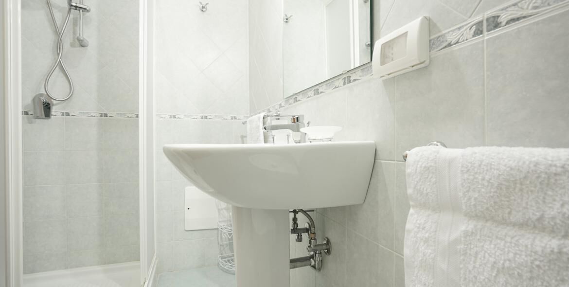 A bathroom with a white sink, a shower, and a towel hanging on the wall.