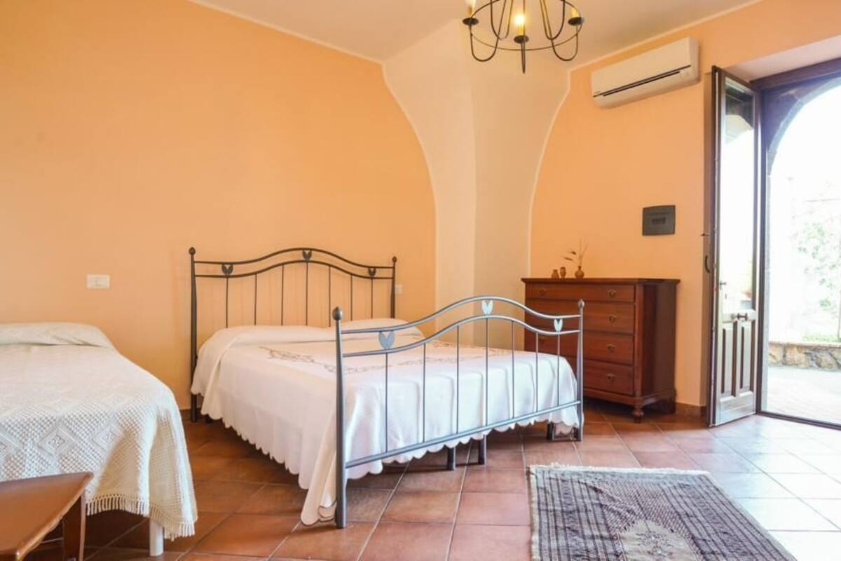 Un dormitorio con dos camas, un aparador de madera, una araña y una puerta que da a un área exterior.