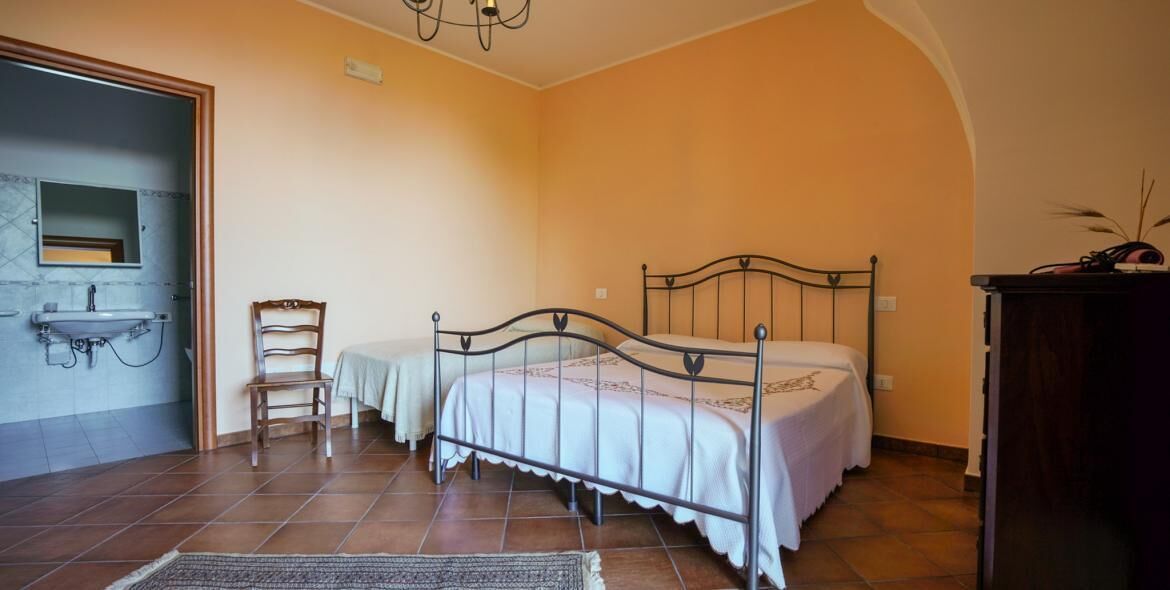 Un dormitorio con cama, una silla, un aparador y una mesita.