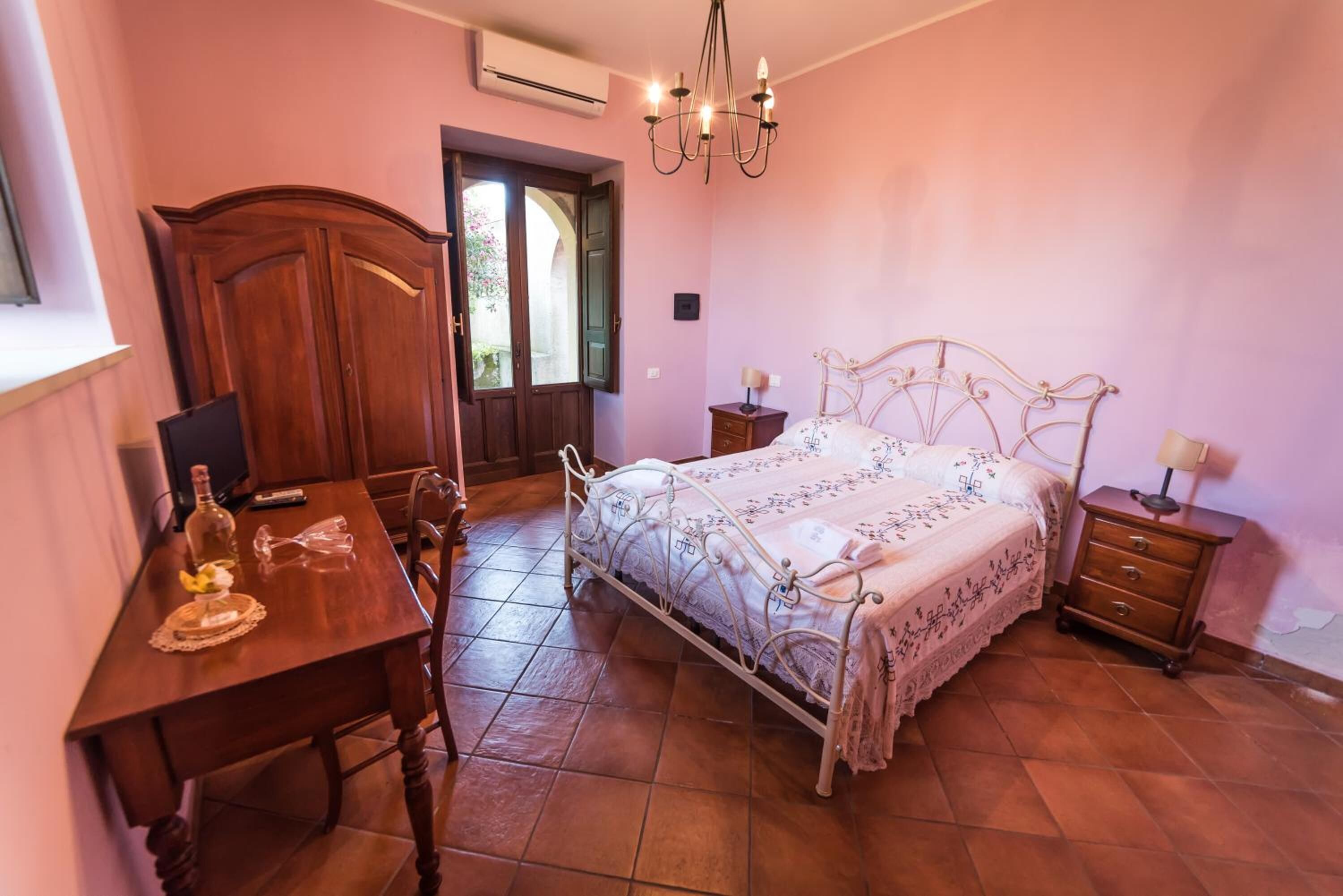 A bedroom with a wooden desk, a bed with a metal frame, and a chandelier.