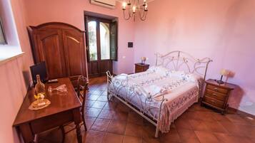 Quarto com escrivaninha de madeira, cama com estrutura de metal e um candelabro.