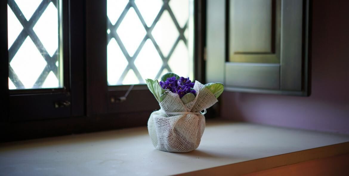 A small, woven basket with purple flowers on a windowsill.