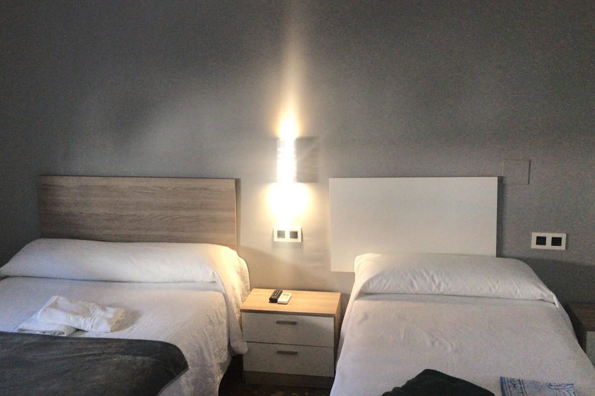 Una habitación de hotel con dos camas, una mesita de noche y un aplique de pared.