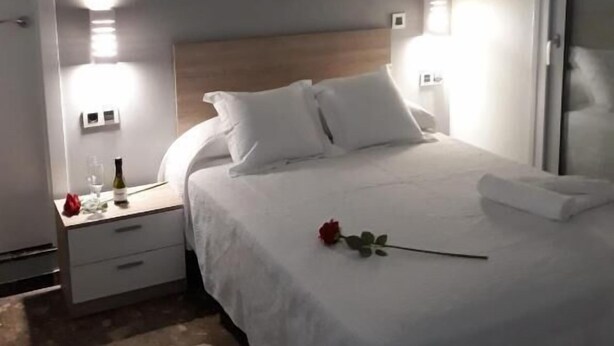 Una habitación de hotel con una cama, una mesita de noche, aire acondicionado de pared y una puerta.