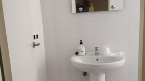 Un baño con un lavabo blanco, un espejo encima y una puerta a la izquierda.