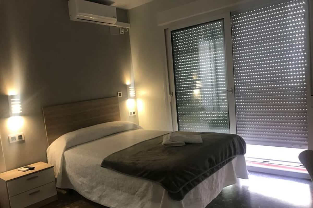 Un dormitorio moderno con cama, mesitas de noche y una ventana con persianas.