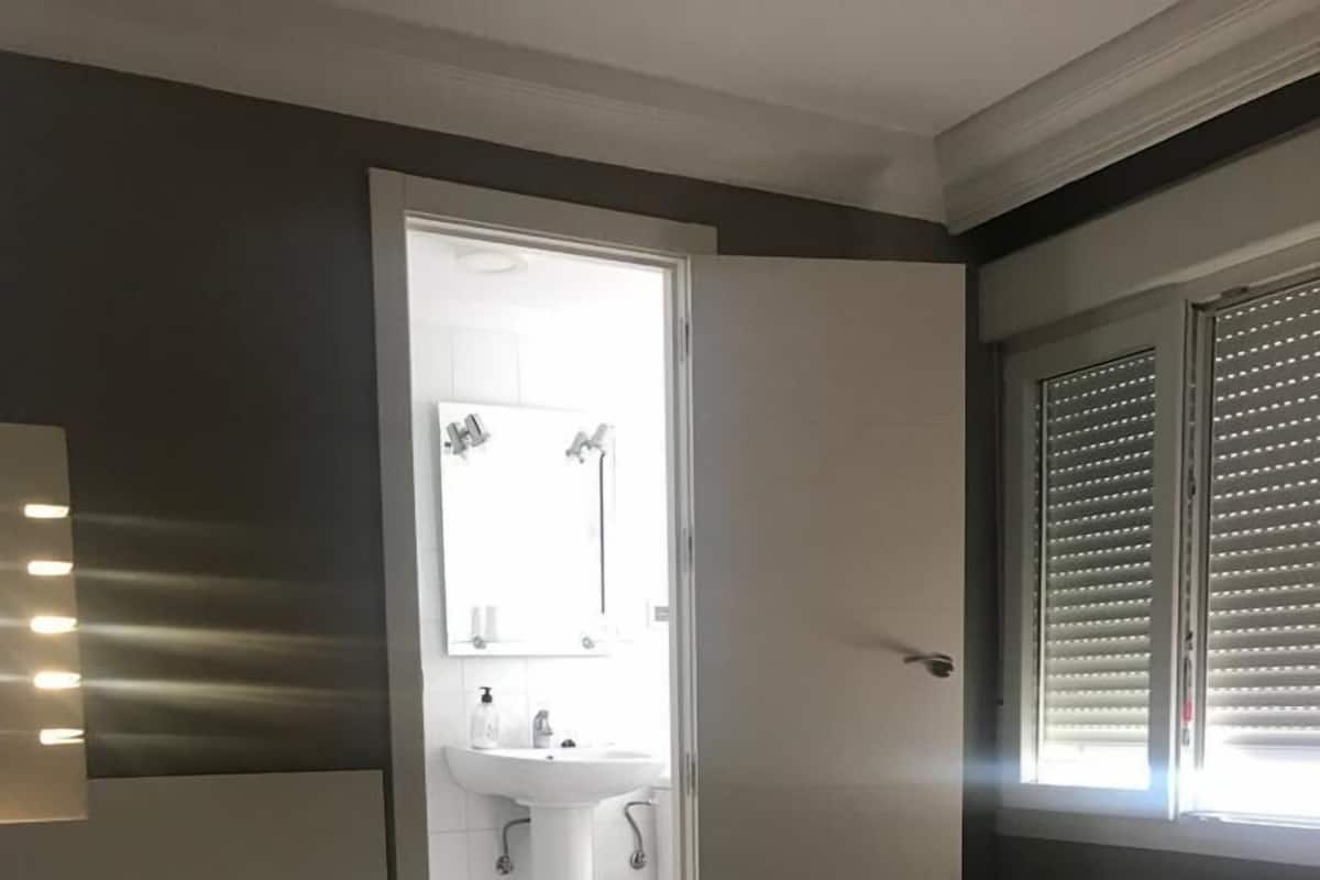 Una habitación de hotel con una cama, un baño visible a través de una puerta abierta y una ventana con persianas.