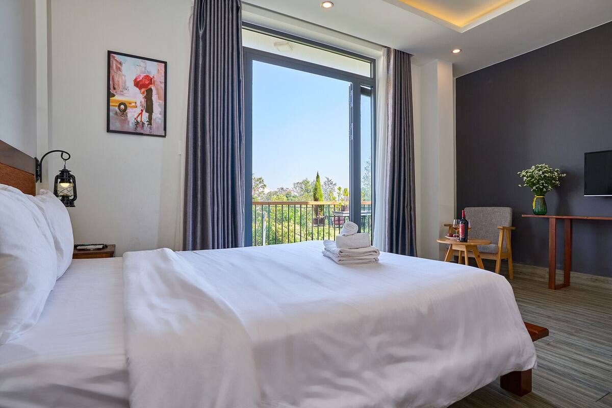 Habitación de hotel con una cama grande, un escritorio con silla, televisión y balcón con vistas.