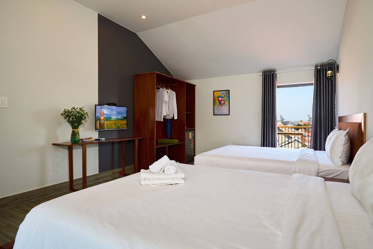 Habitación de hotel con dos camas, un televisor, un escritorio con una planta y vistas al exterior.