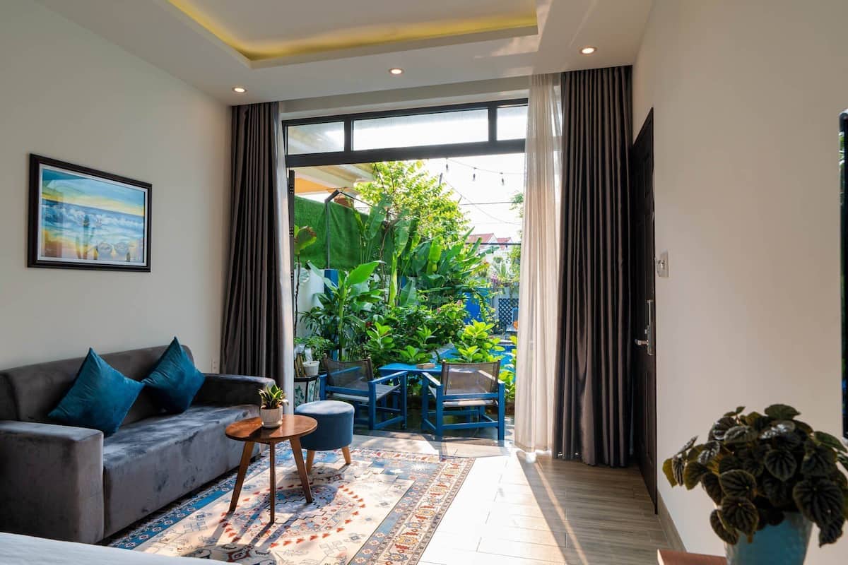 Una sala moderna con un sofá gris, cojines azules, una mesita redonda con una planta y una alfombra colorida.