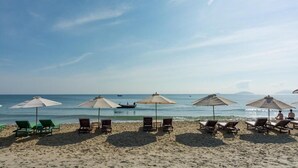 A beach with rows of sun loungers and umbrellas, a clear sky, and calm sea. - MQ Villa (Da Nang)