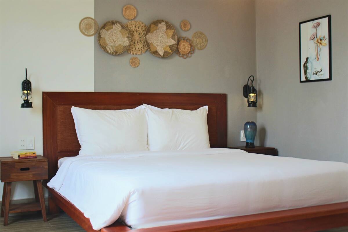 Una cama bien hecha con sábanas blancas, cabecera de madera y dos mesitas de noche con lámparas.