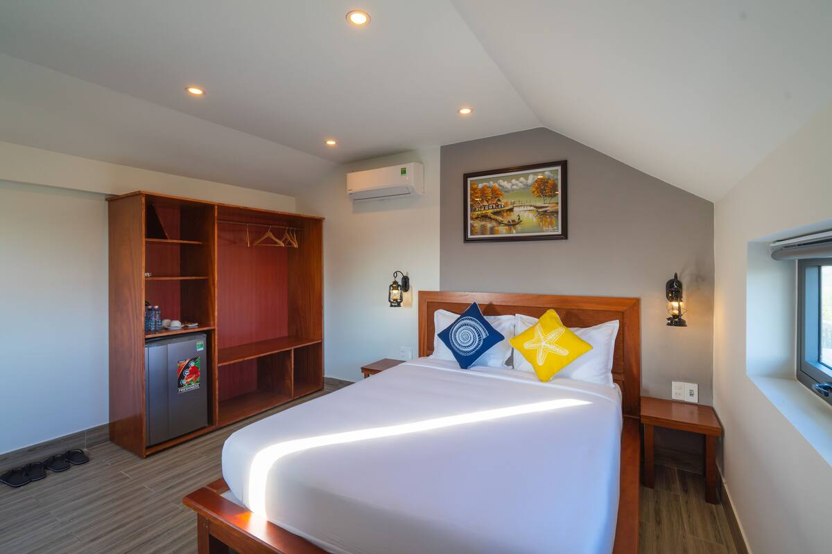 Una habitación de hotel con una cama grande, un armario, un refrigerador pequeño y un cuadro en la pared.