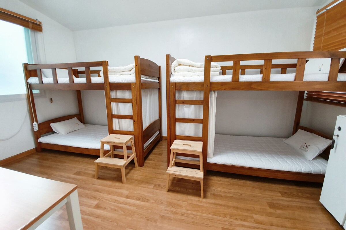 A room with three bunk beds, each with a wooden ladder and a small wooden stool. There is a white table in the foreground.
