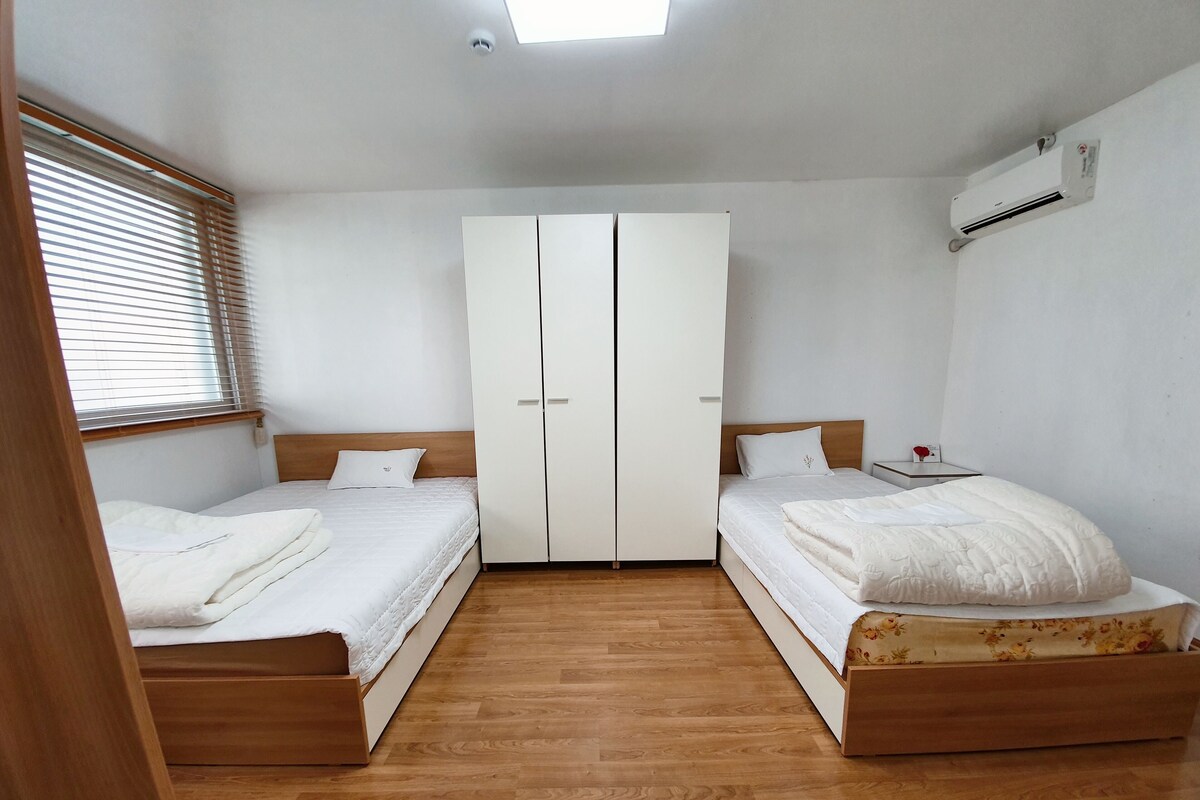A bedroom with two beds, a wardrobe, and an air conditioning unit.