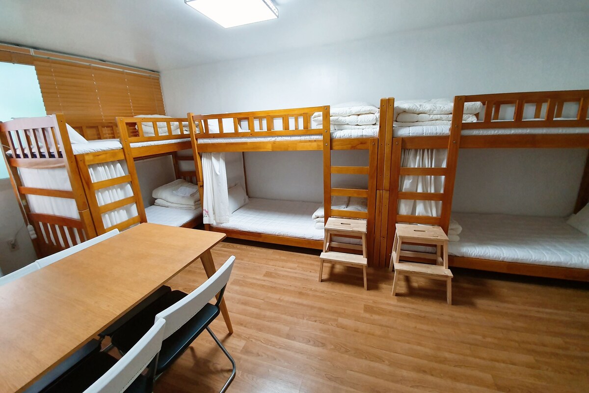 A dormitory room with bunk beds, a desk, and a chair.
