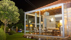 Un espace de restauration extérieur, à moitié fermé par des parois de verre, avec des murs en pierre, du mobilier en bois et un éclairage d’ambiance.