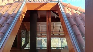 Une chambre moderne aménagée sous les toits, avec un plafond en pente, des poutres en bois et une verrière.