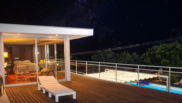 Une terrasse extérieure moderne avec une piscine, des chaises longues et un espace chambre clos par des baies vitrées.