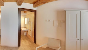 Een gang met een witte kast, een rieten stoel en een deur naar een badkamer.