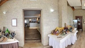 Een ruime kamer met een hoge plafond en zichtbare houten balken, met een stenen muur, een trap naar een ander niveau en een tafel gedekt met eten en drinken.