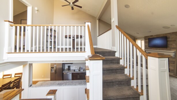 A multi-level home interior with a staircase, kitchen, dining area, and a TV mounted on a stone wall. - Ski Home with Hot Tub and King Beds (Sandy)