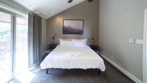 A bedroom with a large bed, a ceiling fan, a window with curtains, a framed picture on the wall, and a nightstand with a lamp. - Ski Home with Hot Tub and King Beds (Sandy)