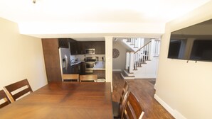 A spacious dining area with a wooden table and chairs, a kitchen in the background, and a staircase leading to another level. - Ski Home with Hot Tub and King Beds (Sandy)