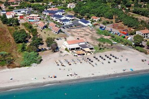 Vista aérea de uma área costeira com praia, vários edifícios e veículos estacionados.