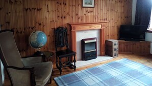 Ein Wohnzimmer mit Holzwandverkleidung, Kamin, Globus, Sessel und Fernseher.