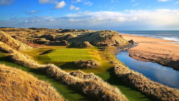 Ein Küsten-Golfplatz mit Sandstrand und einem Wasserkörper.