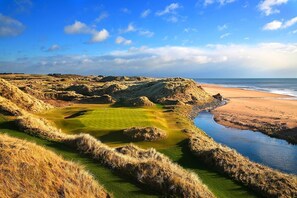 Un campo de golf costero con playa arenosa y extensión de agua.