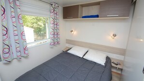 A bedroom with a bed, curtains, bedside tables, and built-in storage. - Camping Le Vieux Colombier (Moustiers-Sainte-Marie)