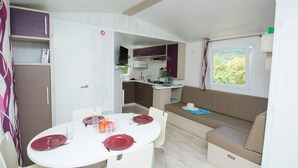 A compact kitchenette with a microwave, stove, and sink, a dining area with a round table and chairs, and a sofa with a window view. - Camping Le Vieux Colombier (Moustiers-Sainte-Marie)