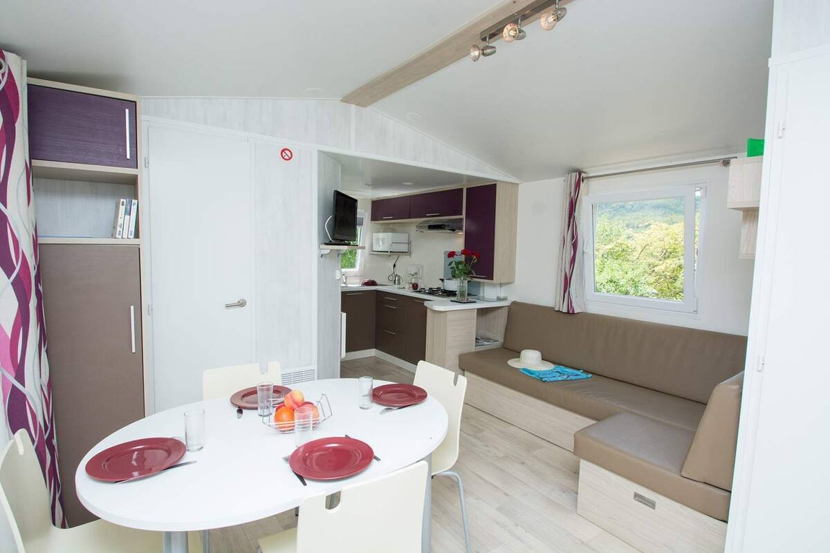 A compact kitchenette with a microwave, stove, and sink, a dining area with a round table and chairs, and a sofa with a window view.