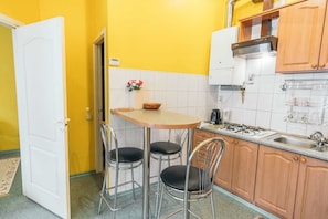 Uma cozinha compacta com porta branca, uma mesa pequena com duas cadeiras e armários de madeira.