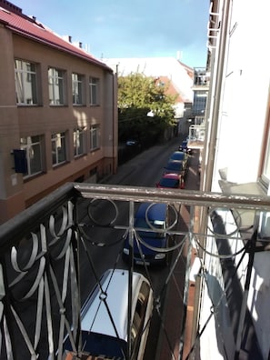 A balcony with a metal railing overlooking a street with parked cars and buildings. - Like Home Apartments (Vilnius)