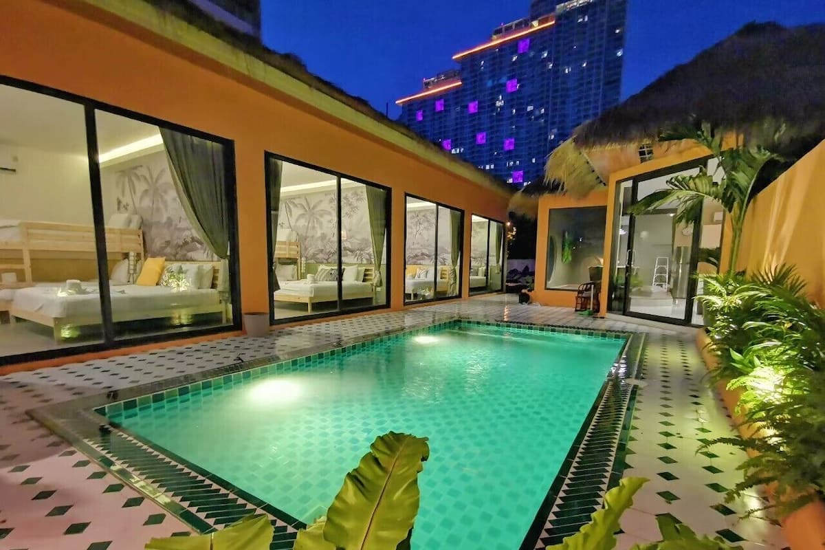 A swimming pool with a tiled edge, surrounded by a building with large windows and a thatched roof structure.