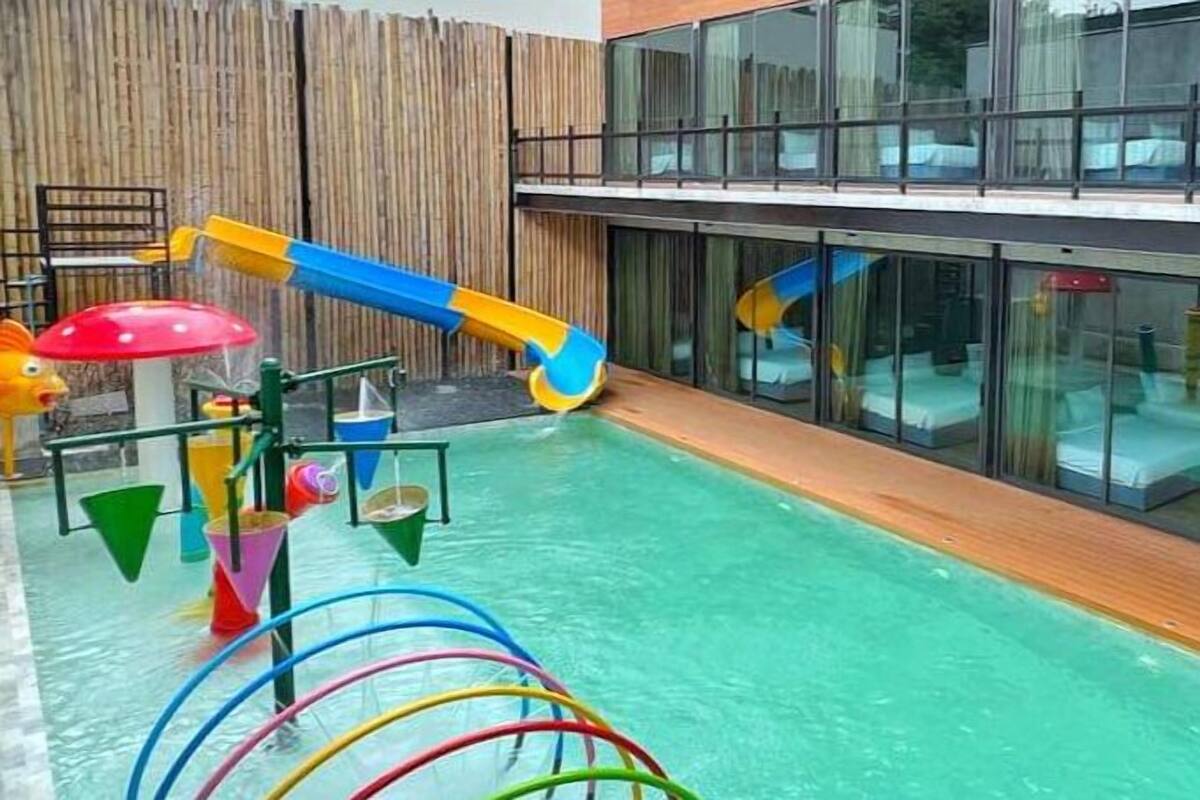 A modern hotel with a rooftop pool area featuring a water slide and play structures.