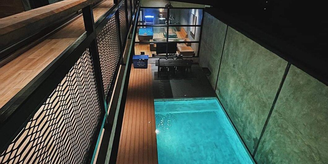 A modern hotel room with a pool, a wooden deck, and a view of the interior.