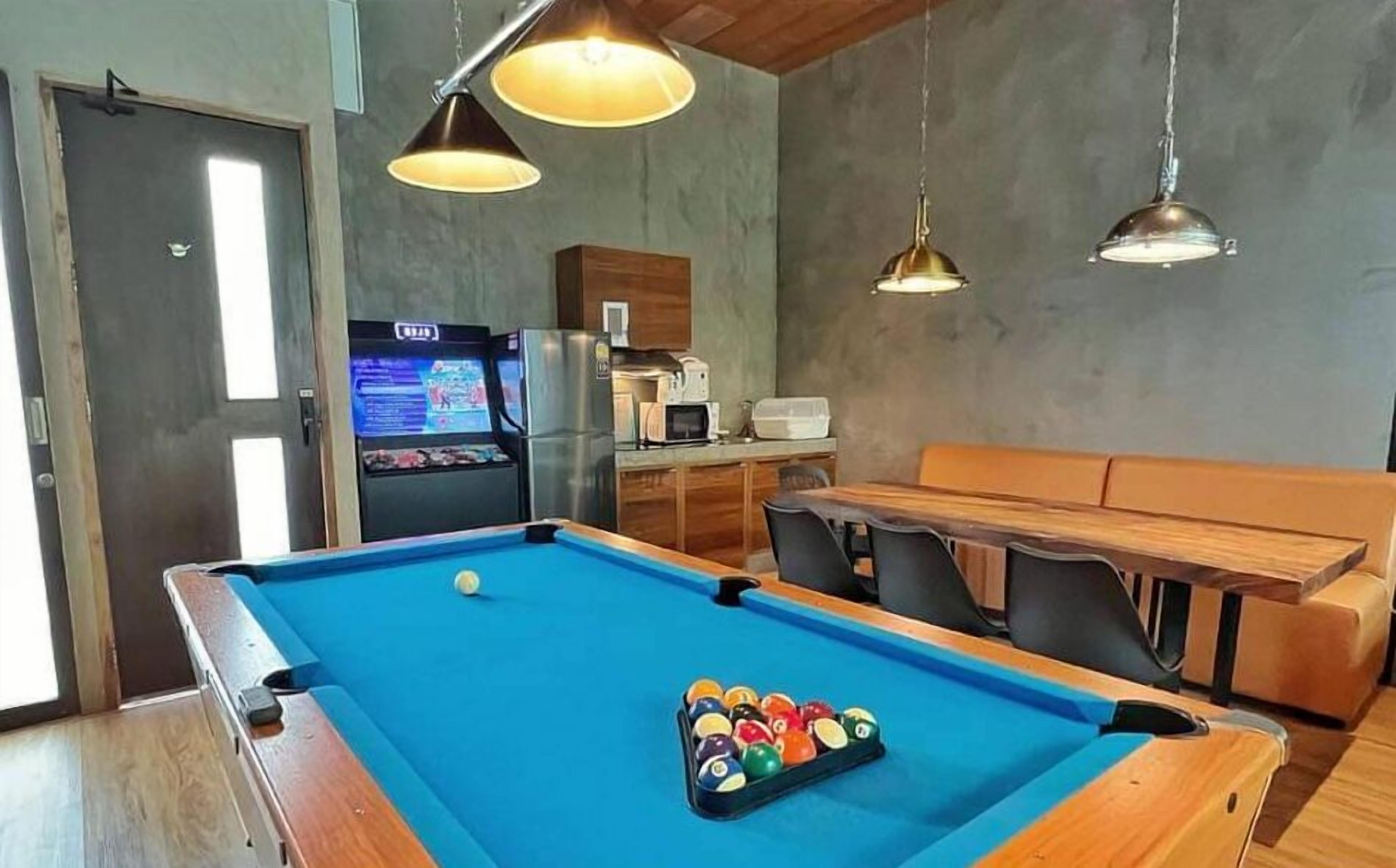 Uma mesa de bilhar com bolas, um frigorífico, um micro-ondas e um espaço de estar com uma mesa e cadeiras.