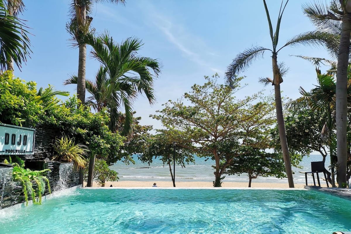 A pool area with clear blue water, surrounded by palm trees and a view of the ocean.