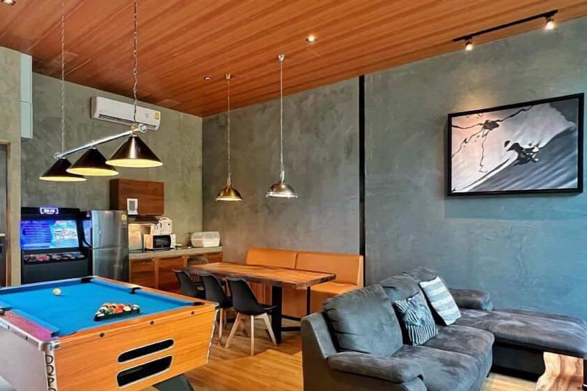 A modern living room with a pool table, a sofa, and a dining area.