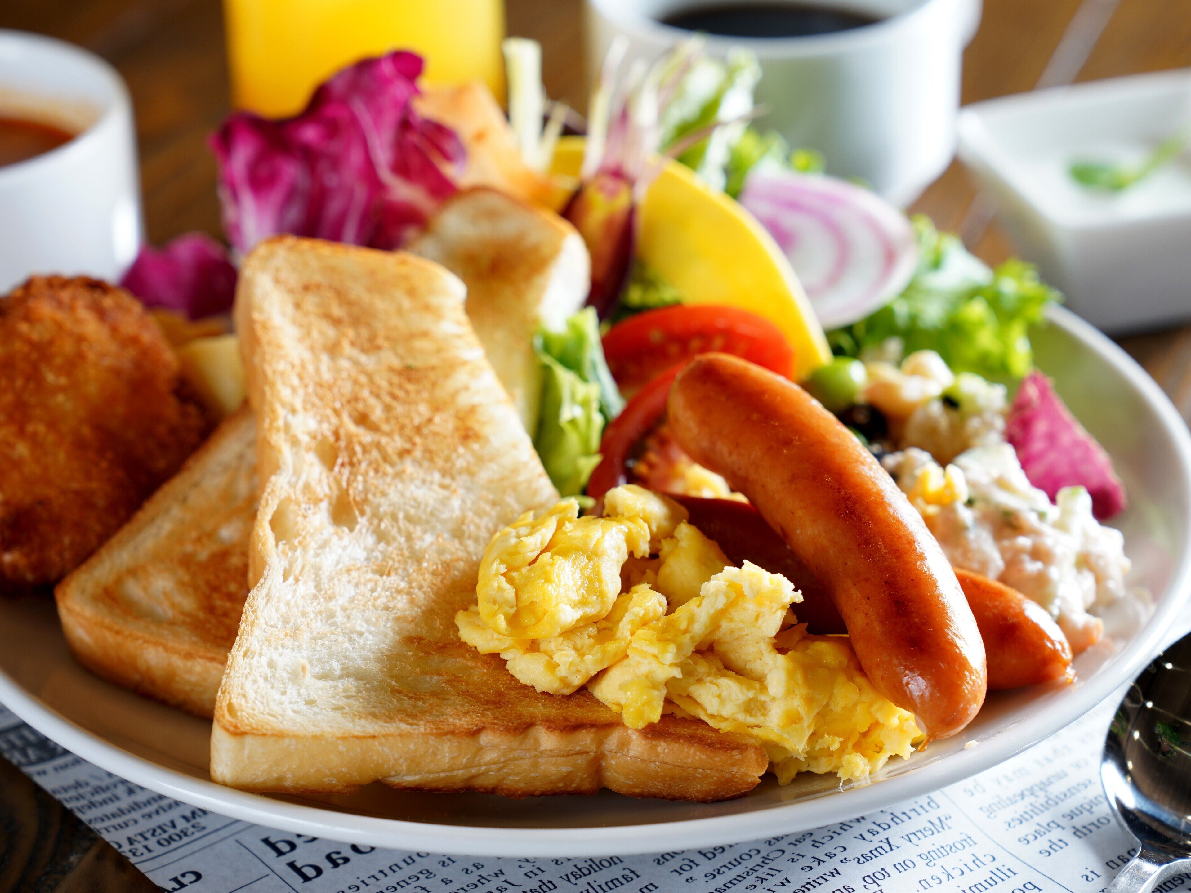 A breakfast plate with toast, scrambled eggs, sausage, and a side salad.