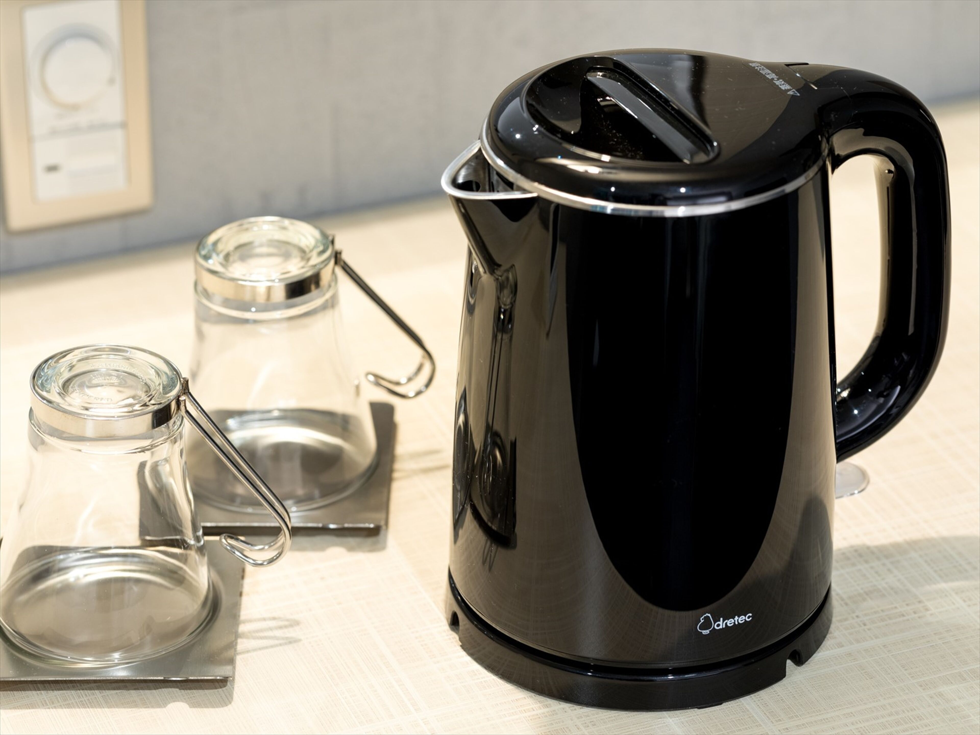 Een zwarte elektrische waterkoker met handvat en tuit, geplaatst op een witte ondergrond naast een heldere glazen pot met een metalen deksel.