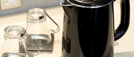 Een zwarte elektrische waterkoker met handvat en tuit, geplaatst op een witte ondergrond naast een heldere glazen pot met een metalen deksel.